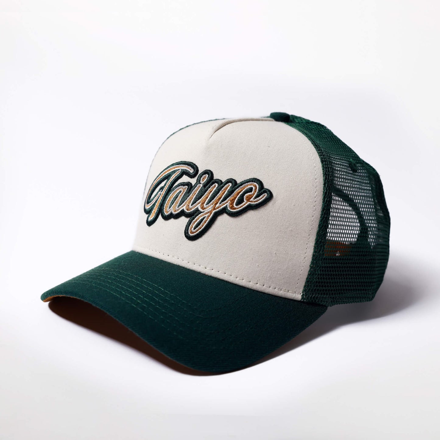 Casquette trucker Taiyo en coton organique beige avec visière en daim marron et filet vert, logo brodé sur le devant.